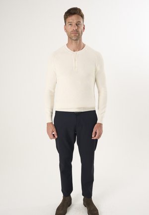Lyscremefarvet langærmet henley-top med struktureret strik, tre-knaps placket, parret med marineblå slim-fit bukser og brune ankelstøvler.