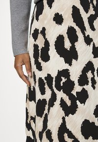 Käsi lepää beige- ja mustavalkoisen abstraktin leopardikuvioisen hameen päällä, yllä harmaa pitkähihaisen paita.