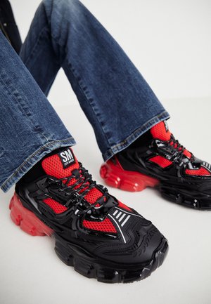 Μαύρα και κόκκινα αθλητικά παπούτσια με δίχτυ, χοντρές διαφανείς κόκκινες σόλες και ανακλαστικές ρίγες. Συνδυασμένα με μπλε τζιν παντελόνι.