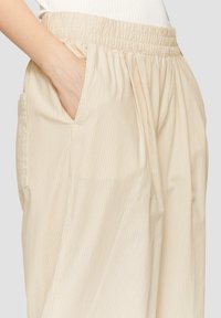 Lichtbeige gestreepte broek met elastische tailleband, zijzakken en een ontspannen pasvorm. De stof lijkt zacht met een gladde textuur.