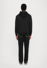 Hoodie preto com capuz ajustável, combinado com jeans escuros com bolsos traseiros distintos. Tecido suave, corte regular. Look casual.