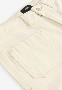 Crème kleurige denim jeans met een soepele textuur, voorzien van een voorzak, contrasterende stiksels en een merklabel op de tailleband.