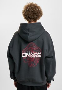 Black oversized hoodie with a red dragon graphic and bold white text "DANGEROUS" on the back. Soft material, featuring a spacious hood.