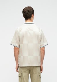 Kortærmet beige polo-shirt med et ternet mønster, der har en sortstribet krave og manchetter, lavet af glat, let stof.