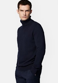 Granatowy sweter z golfem, wykonany z dzianiny, z prążkowanym kołnierzem i brzegiem. Posiada małe logo na klatce piersiowej oraz dopasowany krój.