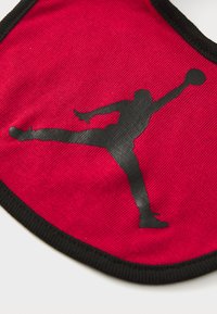 Red fabric face mask with a black Jumpman logo, featuring a textured surface and a contrasting black border.
