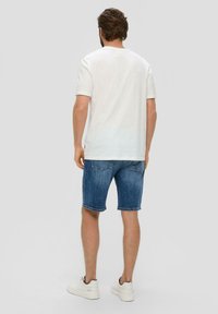 Biała koszulka z krótkim rękawem w połączeniu z niebieskimi szortami dżinsowymi. Szorty mają podwinięty dół i tylne kieszenie. Całość uzupełniają białe sneakersy.