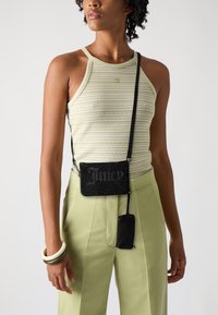 Borsa a tracolla nera con perline e testo "Juicy", abbinata a pantaloni plissettati verde chiaro e a un top senza maniche a strisce.