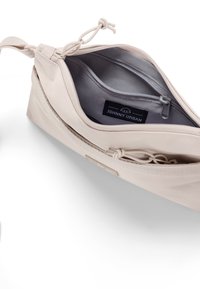 Borsa di stoffa beige con una texture liscia, dotata di una cerniera grigia e di una tasca interna. Etichetta con il logo visibile all'interno. Chiusura a coulisse nella parte superiore.