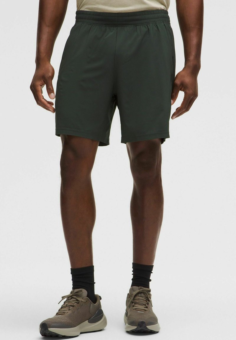 Pantalones cortos deportivos de color verde oscuro con una cinturilla elástica, textura suave y un corte relajado, combinados con zapatillas deportivas de malla beige y calcetines negros.