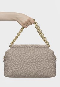 Beżowa torebka o teksturowanym, puszystym wzorze z nieregularnymi kształtami, ze złotym metalowym uchwytem w formie łańcucha oraz zamkiem błyskawicznym po bokach.