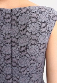 Robe en dentelle grise avec des motifs floraux, dotée d'un col rond et de manches courtes. Fermeture éclair au dos. Tissu texturé avec des détails transparents.