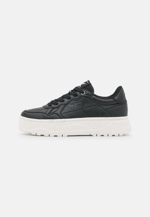 Zwarte lage sneaker met een dikke witte zool, zwarte veters en subtiel logo aan de zijkant, gezien vanaf de buitenkant.