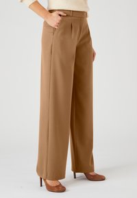 Khaki wijde broek met plooien, riemlussen en zijzakken. Gladde stof met een getailleerde pasvorm, gecombineerd met bruine hakken.