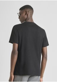 Camiseta de algodón negra con mangas cortas, cuello redondo y un corte relajado. Textura suave y diseño minimalista, mostrada desde la parte de atrás.