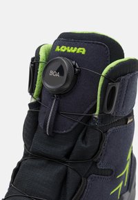 Donkerblauwe boot met groene accenten, textielstof en een zwart BOA-sluitsysteem voor aanpassing. Voorzien van een gewatteerde kraag en versterkte delen.
