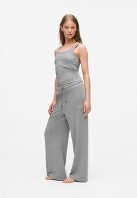 Top senza maniche grigio e pantaloni ampi coordinati realizzati in tessuto morbido; presenta una vita con coulisse e un logo ricamato sul top.