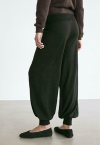 Schwarze, locker sitzende Hose mit enger zulaufendem Bein, geripptem Bund und Bündchen. Kombiniert mit schwarzen, flachen Slip-on-Schuhen. Glatte Textur.