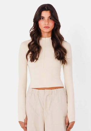 Maglione beige a maniche lunghe con collo alto, dotato di una zip frontale e di un design cropped, realizzato in un tessuto morbido ed elasticizzato.