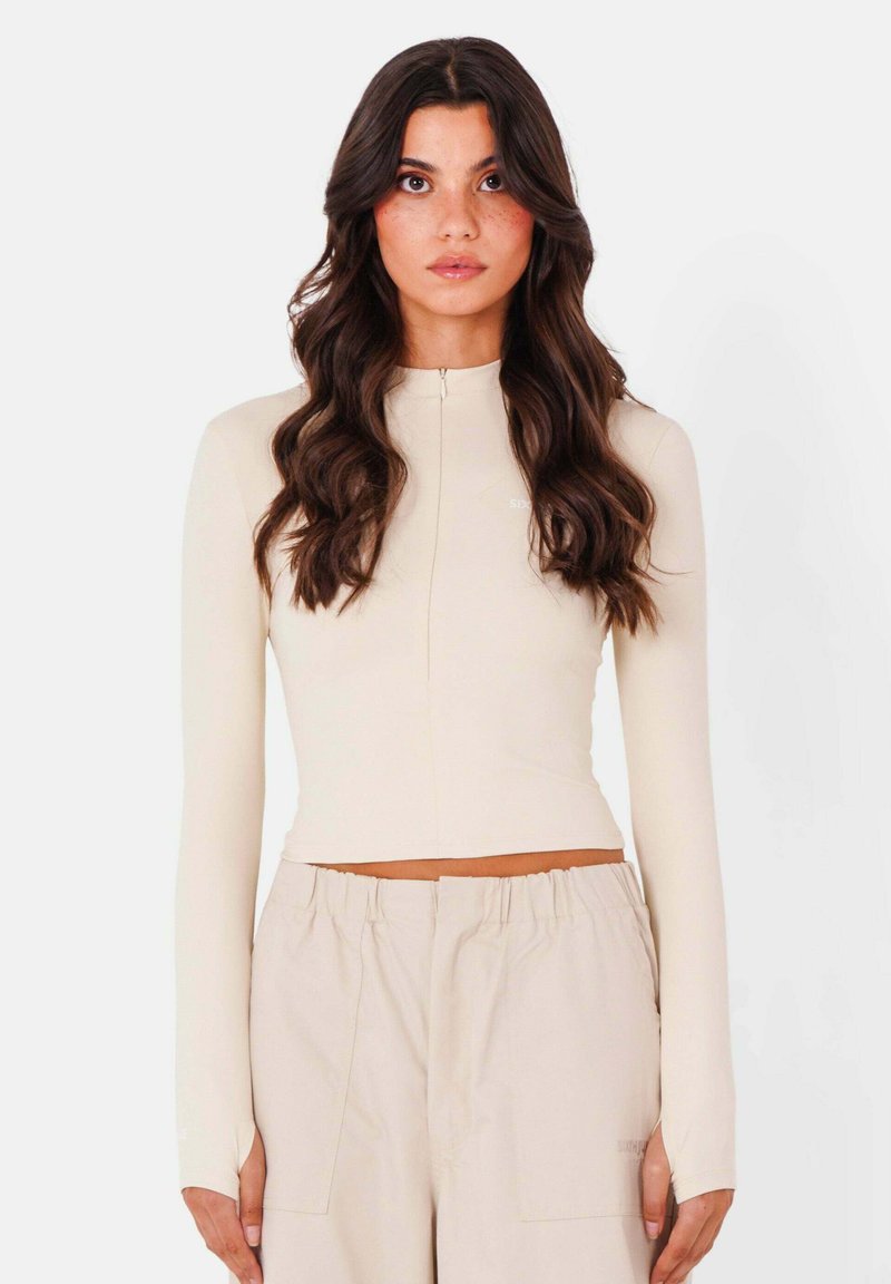 Maglione beige a maniche lunghe con collo alto, dotato di una zip frontale e di un design cropped, realizzato in un tessuto morbido ed elasticizzato.