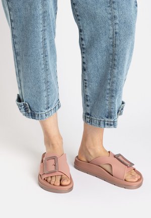 Rosenrote Gummisandalen mit einem breiten Riemen und einer metallischen Schnalle sowie einer dicken Sohle. Getragen mit leicht blauen, hochgekrempelten Jeans.