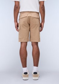 Tan cargo shorts med fire lommer, med lige snit og syet detalje på bagsiden. Bæres med hvide sokker og beige sko.