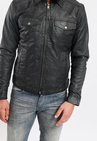 Černá kožená bunda s předním zipem, dvěma náprsními kapsami a patentkami. Hladká textura, přiléhavý střih a mírně opotřebovaný vzhled.