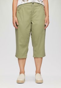 Pantalons cropped vert olive avec une coupe décontractée, dotés de poches avant et d'un ourlet retroussé. Portés avec des chaussures slip-on de couleur claire.