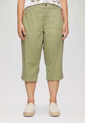 Olijfgroene cropped broek met een relaxed fit, voorzien van voorzakken en een omgeslagen zoom. G gedragen met lichtgekleurde instap schoenen.