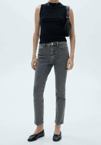 Czarny top bez rękawów, szare jeansy z wysokim stanem i czarne płaskie buty. Jeansy mają lekko zblakłą fakturę i pięć kieszeni.