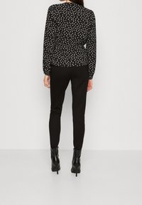 Czarna bluzka z długim rękawem w biały kwiatowy wzór, z fakturowanej tkaniny, z marszczonym pasem, zestawiona z dopasowanymi czarnymi spodniami i botkami na obcasie.