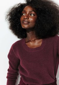 Pull en maille bordeaux avec un col rond et des manches longues, featuring une texture côtelée et une coupe décontractée.