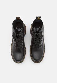 Svarta läderankelboots med gula sömmar, rund tå och snörningsdesign. Har vadderad krage och gummisula. Logotyp på innersulan.