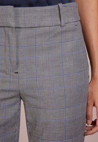 Pantalon à carreaux gris mêlant différents motifs, accents bleus, texture lisse et coupe ajustée avec passants pour ceinture à la taille.