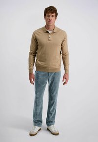 Beige gebreide pullover met drie knopen, gecombineerd met geribde teal broek en witte sneakers. Soepele textuur en relaxte pasvorm door het geheel.
