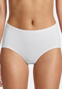 Frau, die schlichte weiße Baumwoll-Slip-Unterwäsche mit hohem Bund trägt, Oberkörper und Oberschenkel sichtbar, vor einem weißen Hintergrund.