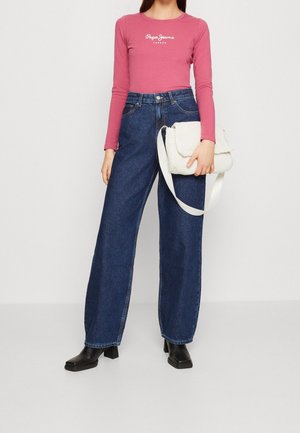 Haut rose à manches longues avec logo blanc, jean bleu taille haute évasé et sac à main blanc texturé avec une bandoulière. Bottes noires à talons.