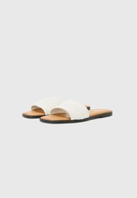Witte gevlochten slidesandalen met een platte zwarte zool en een tan voetbed. Beschikt over twee brede banden aan de bovenkant voor een veilige pasvorm.