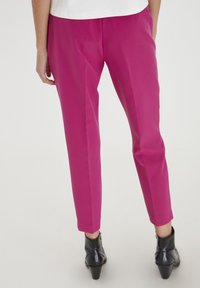 Eri pöllöt, vaaleanpunaiset housut, joissa on sileä pinta, kapenevat lahkeet ja huomaamattomat sivutaskut, yhdistettynä mustiin nilkkureihin.