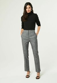 Schwarzes Rollkragenoberteil mit langen Ärmeln, kombiniert mit grauen karierter Slim-Fit-Hosen. Bemerkenswerte Details sind seitliche Taschen und eine taillierte Passform.
