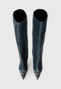Botas vaqueras hasta la rodilla con puntera puntiaguda y detalle de hebilla plateada en el tobillo. Textura suave con un acabado azul desgastado.