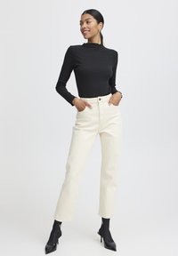 Top negro de manga larga con canalé y cuello alto, combinado con pantalones rectos de talle alto de color crema y tacones negros de punta.