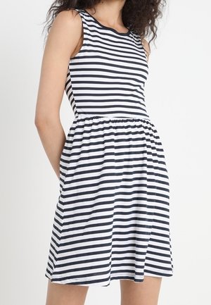 Femme portant une robe sans manches noire et blanche à rayures horizontales, avec une taille cintrée et une jupe évasée.