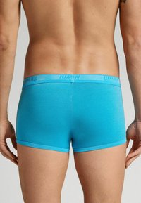 Blå stretchtygs boxerkalsonger med en logotypad elastisk midjeband, med en slät struktur och figursydd design, sedd från baksidan.