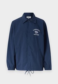Veste boutonnée bleu marine avec col, poignets élastiques, ourlet à cordon de serrage, poches latérales et logo blanc "Carhartt Wip Eightynine" sur la poitrine.