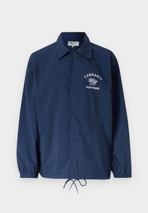 Veste boutonnée bleu marine avec col, poignets élastiques, ourlet à cordon de serrage, poches latérales et logo blanc "Carhartt Wip Eightynine" sur la poitrine.