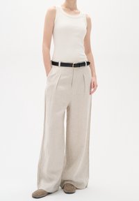 Linneblandade byxor i ljusbeige, med en avslappnad passform, framfickor och ett svart bälte med en guldfärgad spänne. Bärs med en vit linne.