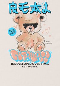 Kreslený medvěd s béžovou srstí, černými slunečními brýlemi a líčky v barvě růžové. Text zní: "Roztomilost se vyvíjí s časem. Není koupena."