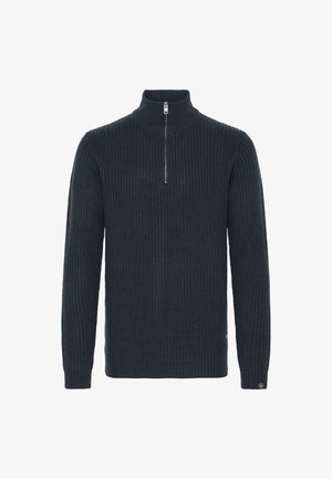 Tummansininen neulepusero, jossa on korkea kaulus ja lyhyt vetoketju. Ominaisuuksiin kuuluu ribbitekstuuri ja pitkät hihat. Pienen logon sijaitsee hihassa.