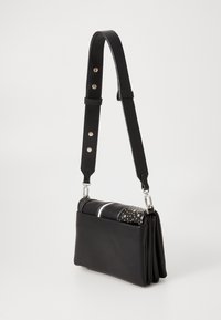 Borsa a tracolla in pelle nera con fronte testurizzato, borchie argentate e due strisce bianche. Tracolla regolabile con hardware argentato. Design compatto.